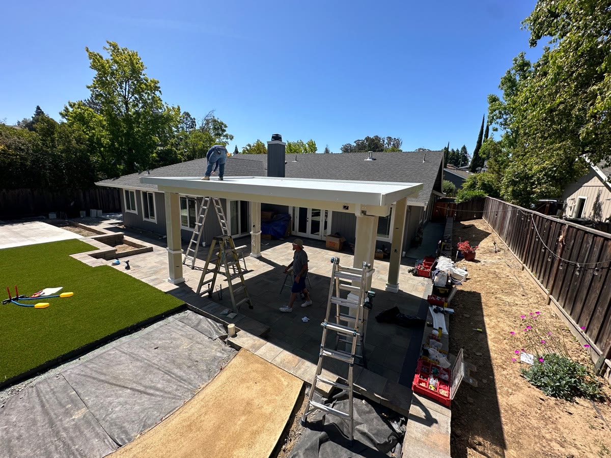 Attached solid patio cover installation over a paver patio and turf backyard by FG Pavers and Turf.