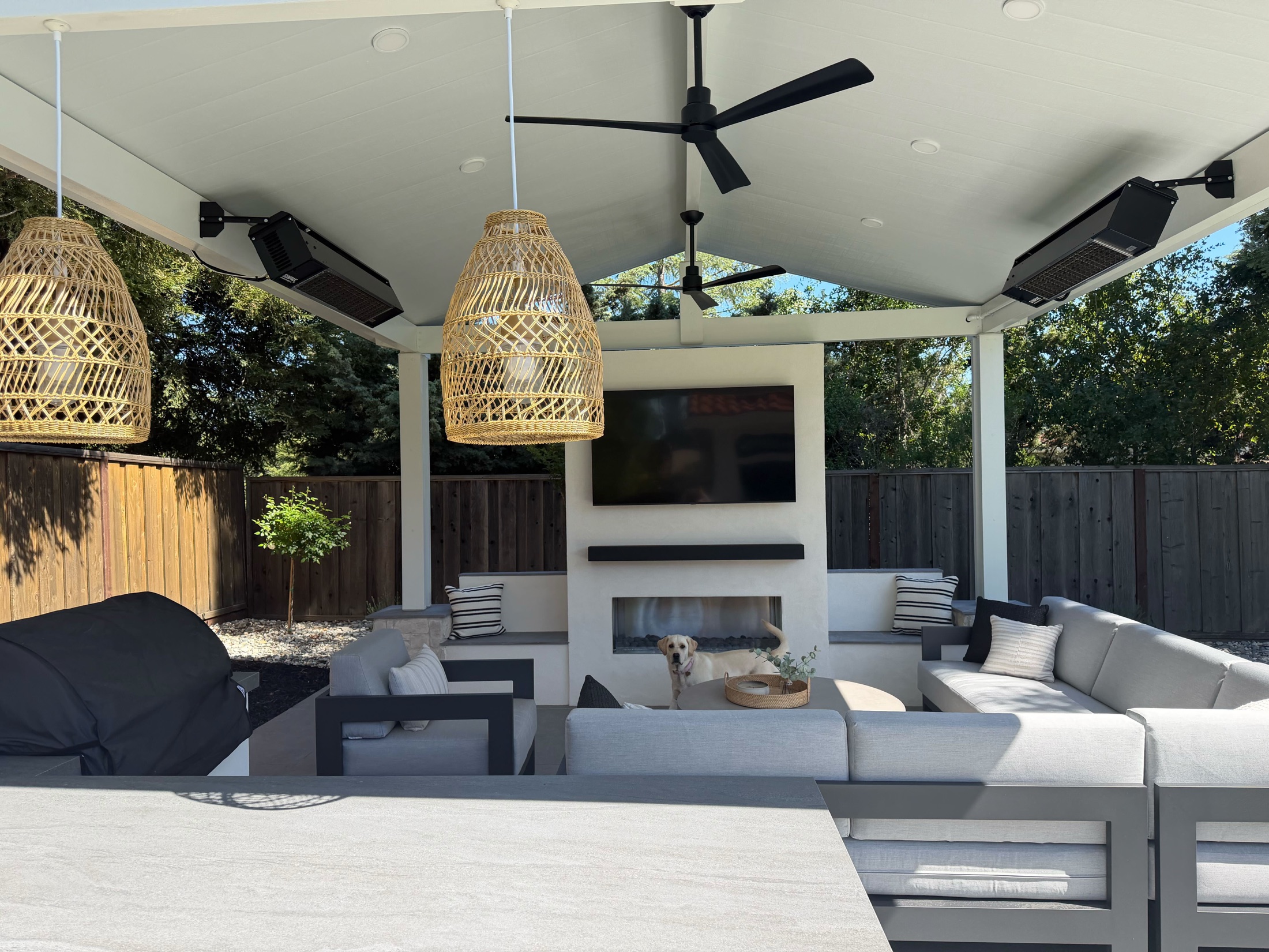 Furnished covered patio with fireplace, pendant lighting, heaters, and lounge seating by FG Pavers and Turf.