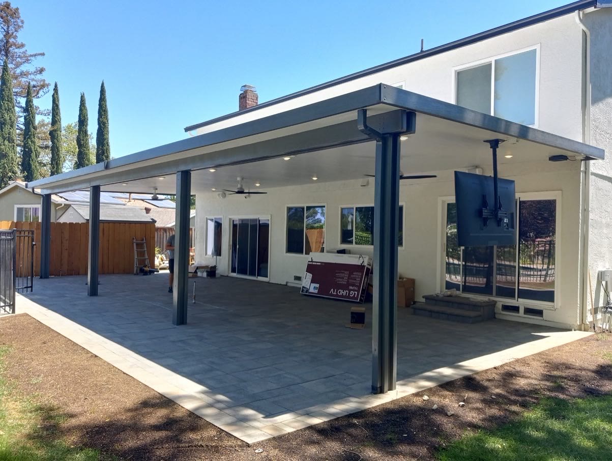 Solid patio cover with slate trim over a backyard patio by FG Pavers and Turf.