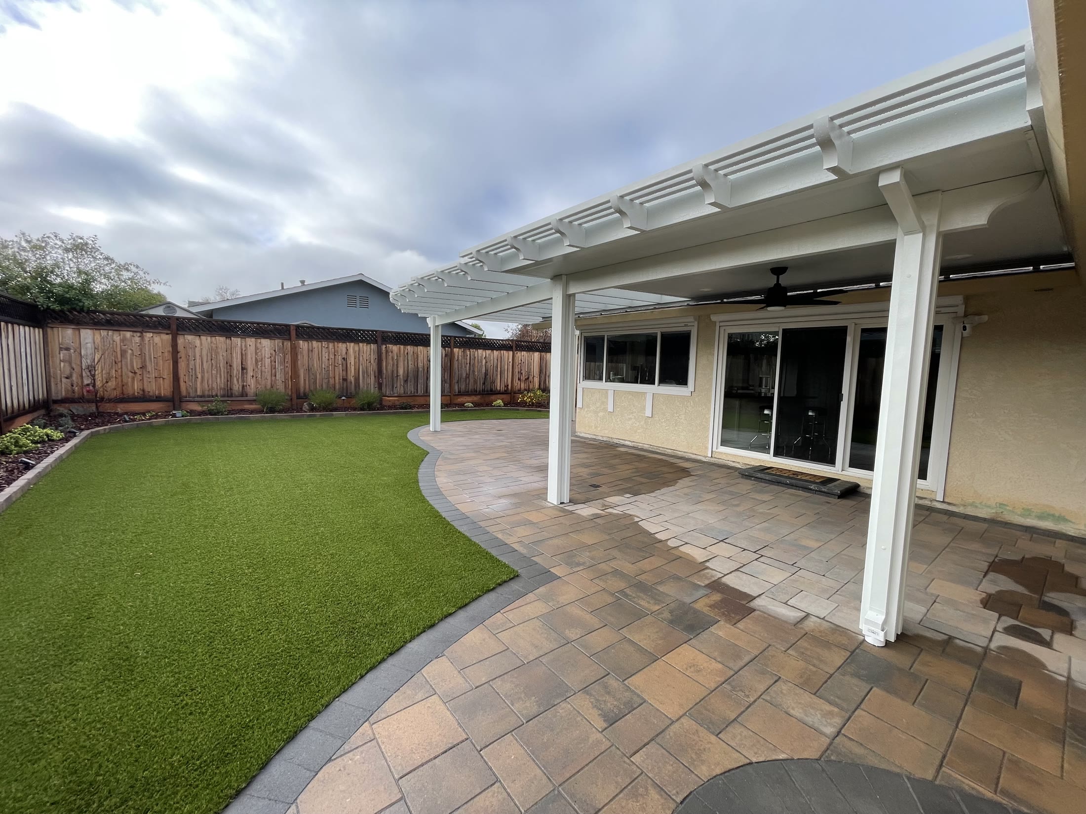 White solid and lattice pergola over a paver patio and turf lawn by FG Pavers and Turf.