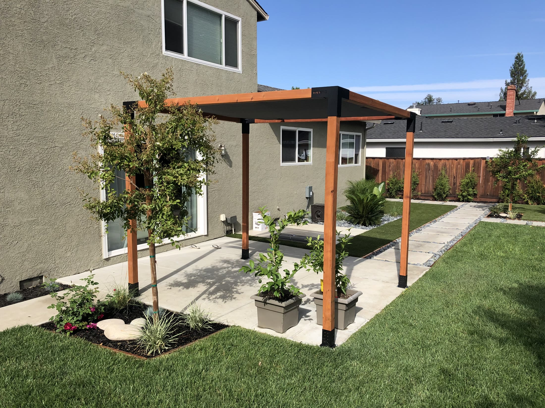 Wood-look freestanding pergola in a finished backyard landscape by FG Pavers and Turf.