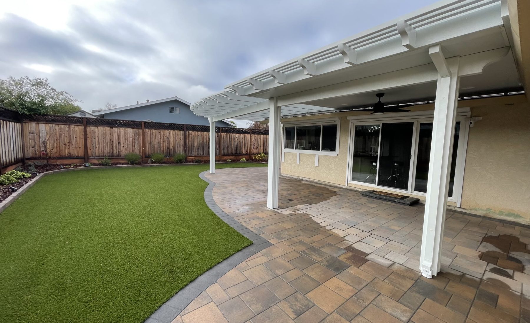 White solid and lattice pergola over a paver patio and turf lawn by FG Pavers and Turf.