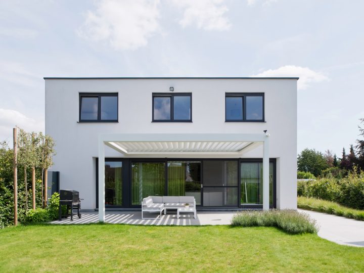 Wall-mounted Pergo Centro SO Classic patio cover with a dark frame and glass wall beside a lawn.