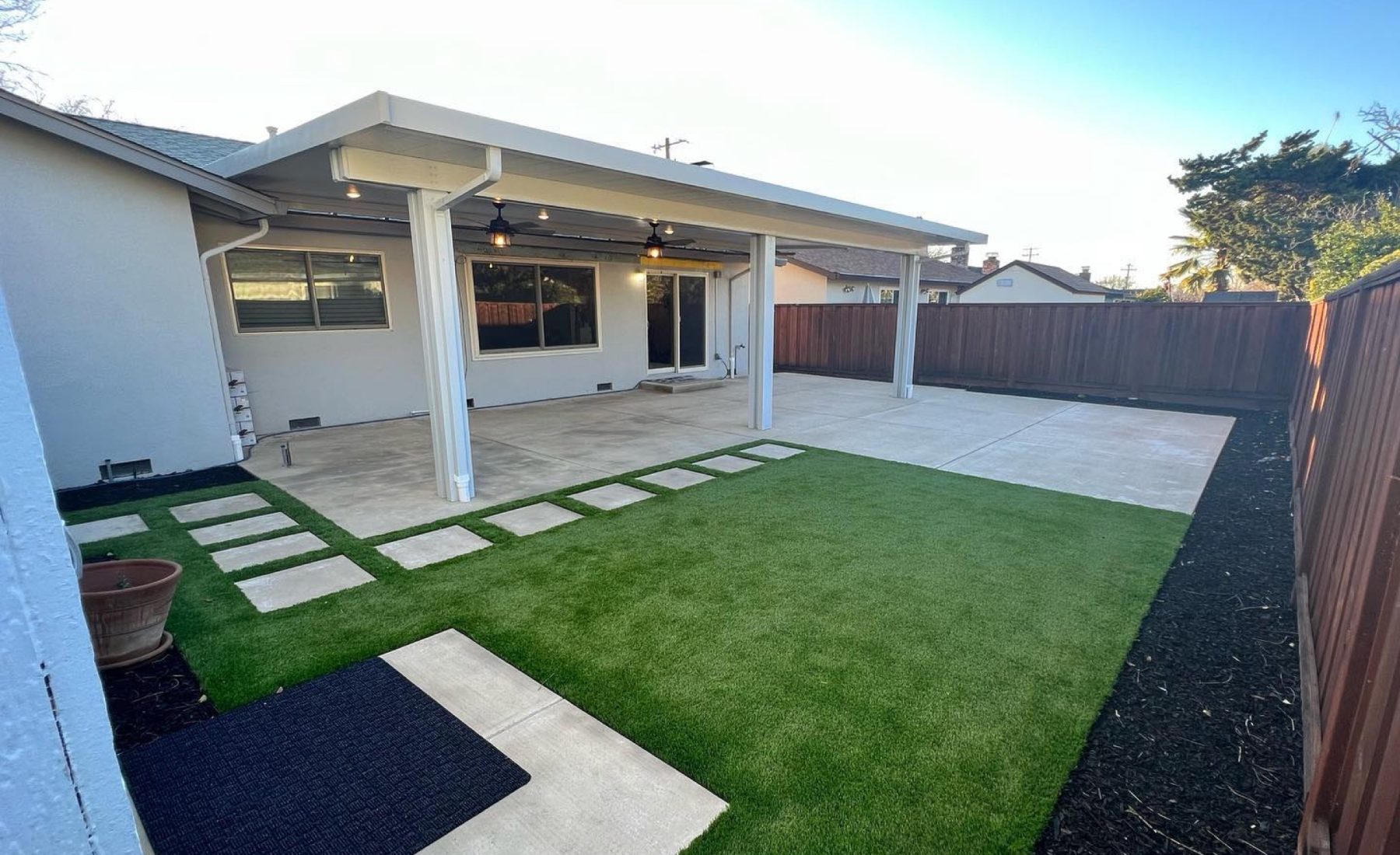 Finished Livermore backyard with a white modern patio cover, concrete patio, turf, and stepper walkway by FG Pavers and Turf.
