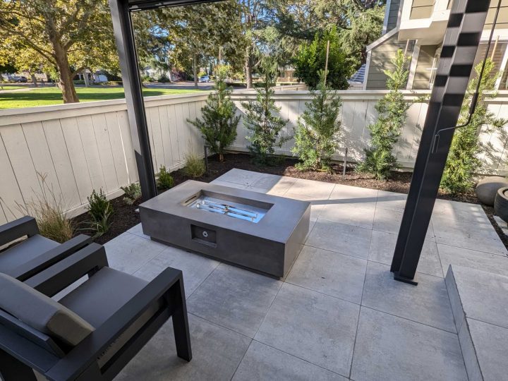 Concrete fire table and planting area beneath a black louvered patio cover in Pleasanton by FG Pavers and Turf.
